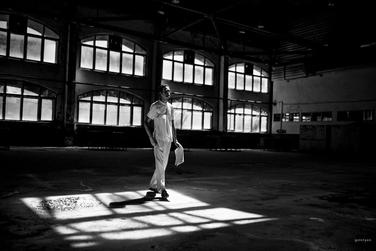 a black and white inage of an artist in a factory interier with a paper in his hands walking.